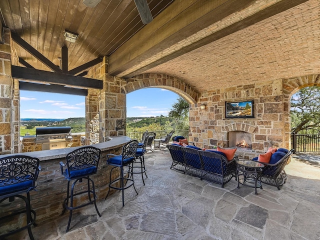 view of patio / terrace with an outdoor living space with a fireplace, a grill, an outdoor kitchen, and a bar