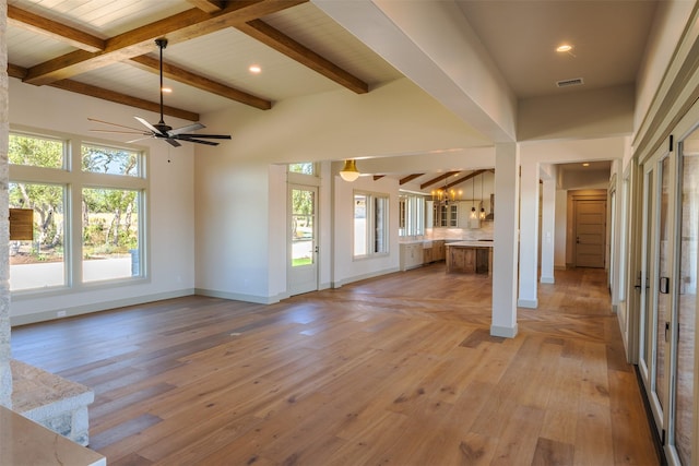 unfurnished living room featuring ceiling fan, plenty of natural light, beam ceiling, and light hardwood / wood-style flooring