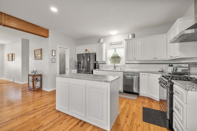 kitchen with a kitchen island, appliances with stainless steel finishes, white cabinets, wall chimney exhaust hood, and light stone counters