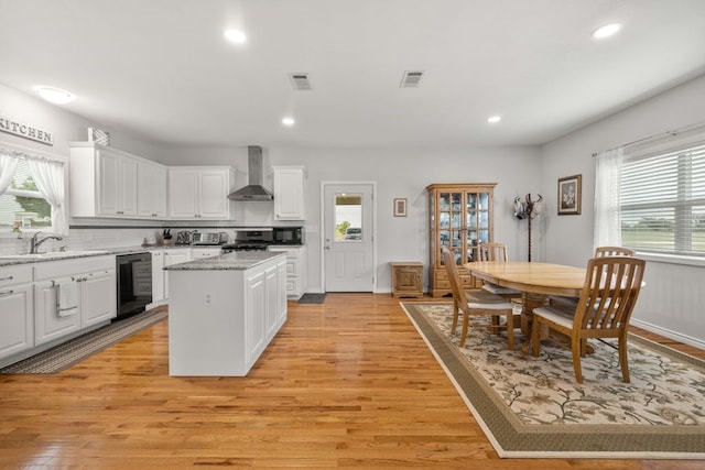 kitchen with a kitchen island, white cabinetry, black dishwasher, light wood-type flooring, and wall chimney exhaust hood