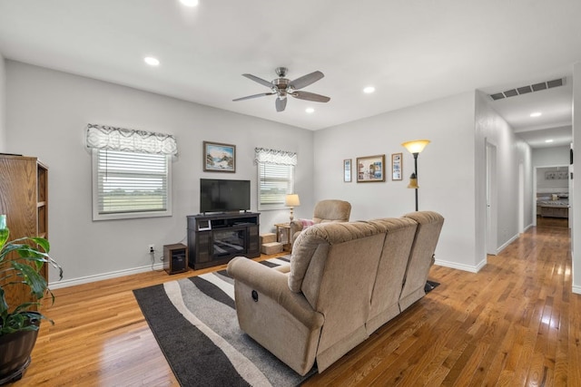 living room featuring light wood-type flooring, ceiling fan, and a fireplace