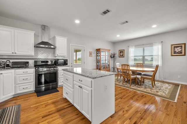 kitchen with a center island, gas stove, white cabinetry, wall chimney range hood, and light hardwood / wood-style floors