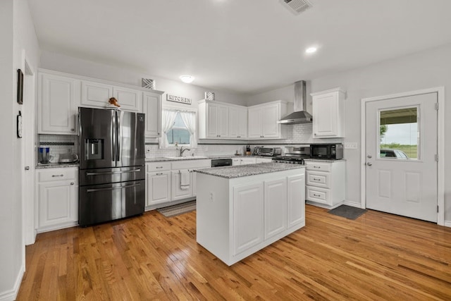 kitchen featuring white cabinets, black appliances, wall chimney exhaust hood, a kitchen island, and light wood-type flooring