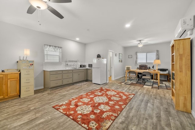 kitchen featuring white refrigerator, sink, a wall unit AC, light wood-type flooring, and ceiling fan