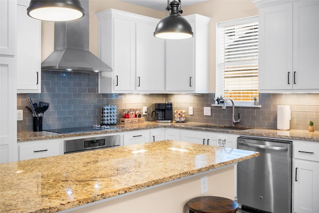 kitchen with appliances with stainless steel finishes, white cabinetry, hanging light fixtures, and wall chimney range hood