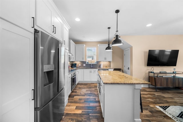 kitchen featuring appliances with stainless steel finishes, a center island, white cabinetry, hanging light fixtures, and light stone counters