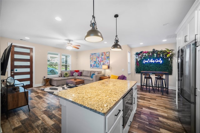 kitchen with white cabinetry, black refrigerator, ceiling fan, a kitchen island, and pendant lighting