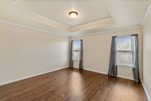 empty room featuring dark wood-type flooring, a tray ceiling, and ornamental molding