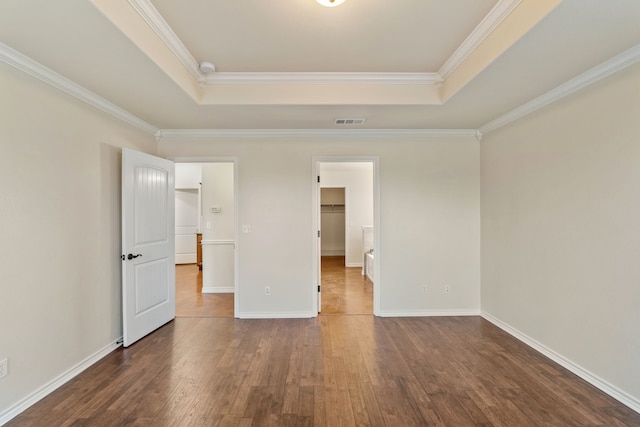 unfurnished bedroom featuring a spacious closet, a tray ceiling, ornamental molding, and dark hardwood / wood-style floors