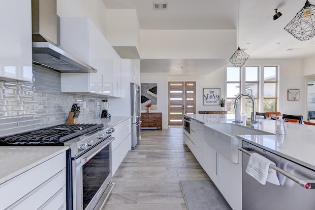 kitchen featuring wall chimney range hood, pendant lighting, sink, stainless steel appliances, and white cabinets