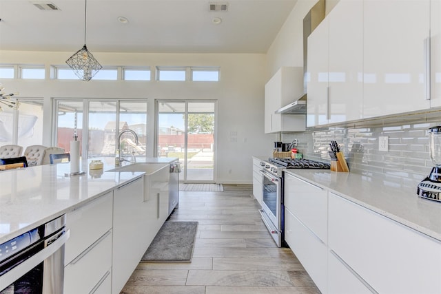 kitchen with extractor fan, high end stove, white cabinetry, hanging light fixtures, and light wood-type flooring