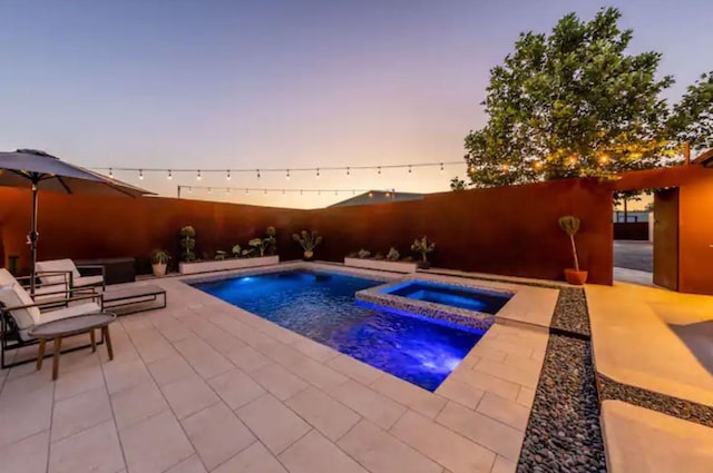 pool at dusk featuring an in ground hot tub and a patio