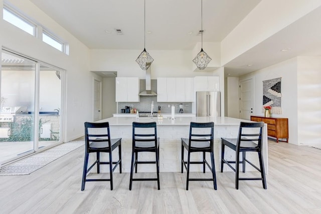 kitchen featuring wall chimney range hood, pendant lighting, high end refrigerator, and white cabinetry