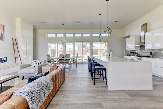 kitchen featuring a kitchen island with sink, wall chimney range hood, white cabinetry, and pendant lighting