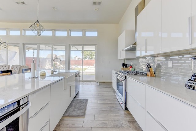 kitchen featuring range hood, pendant lighting, light hardwood / wood-style flooring, stainless steel range, and white cabinets