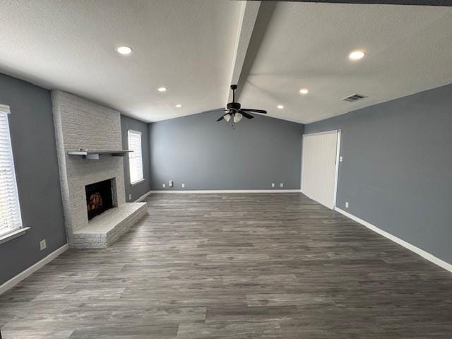 unfurnished living room featuring ceiling fan, dark hardwood / wood-style flooring, lofted ceiling with beams, and a fireplace