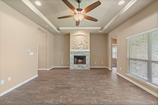 unfurnished living room with ceiling fan, a stone fireplace, crown molding, and a tray ceiling