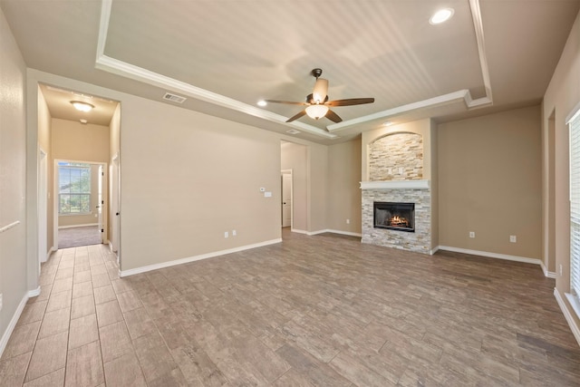 unfurnished living room featuring ceiling fan, crown molding, a raised ceiling, and a stone fireplace