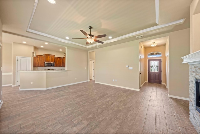 unfurnished living room featuring ceiling fan, a tray ceiling, crown molding, and a fireplace