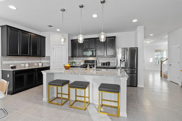 kitchen with decorative light fixtures, black appliances, decorative backsplash, an island with sink, and light tile patterned floors