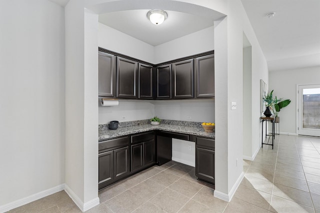 kitchen with light tile patterned floors, built in desk, dark brown cabinets, and light stone countertops