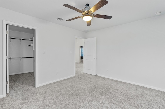 unfurnished bedroom featuring ceiling fan, a walk in closet, a closet, and light colored carpet