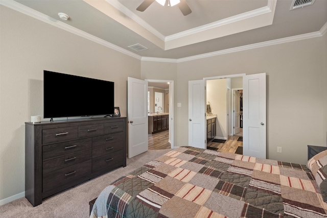 bedroom featuring light carpet, visible vents, ensuite bath, a tray ceiling, and a sink