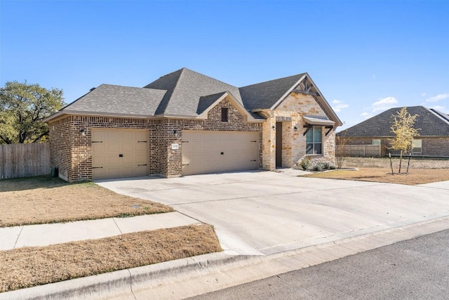 french country inspired facade featuring brick siding, a shingled roof, fence, a garage, and driveway