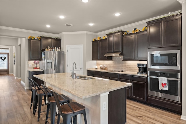 kitchen featuring light wood finished floors, stainless steel appliances, a sink, light stone countertops, and under cabinet range hood