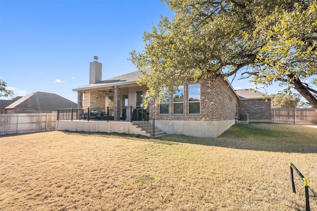 back of property with brick siding, a chimney, a lawn, fence private yard, and cooling unit