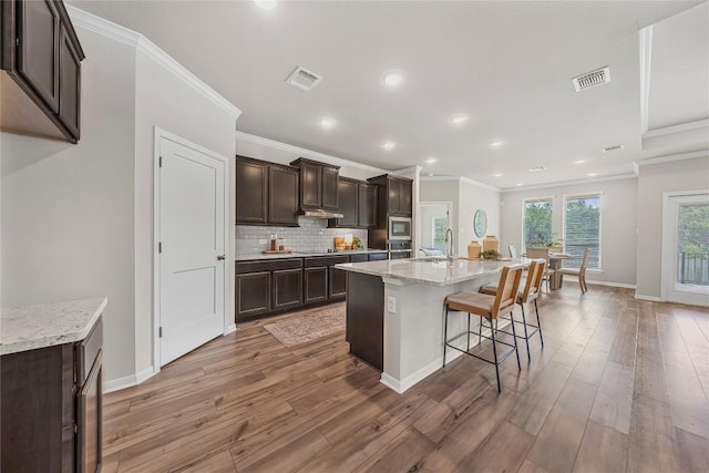 1207 Haley Ln, Salado, TX 76571 - kitchen with crown molding, stainless steel microwave, light wood finished floors, backsplash, and dark brown cabinets