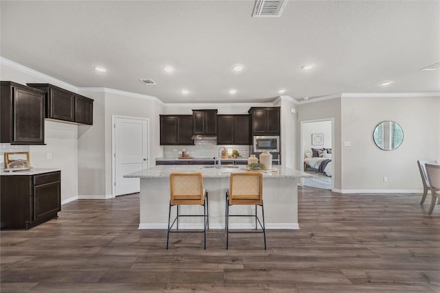 1207 Haley Ln, Salado, TX 76571 - kitchen with stainless steel microwave, an island with sink, backsplash, dark brown cabinets, and crown molding