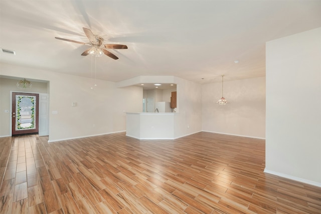 unfurnished living room featuring ceiling fan with notable chandelier and light wood-type flooring