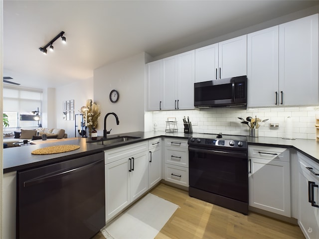 kitchen with white cabinetry, light hardwood / wood-style floors, tasteful backsplash, black appliances, and sink