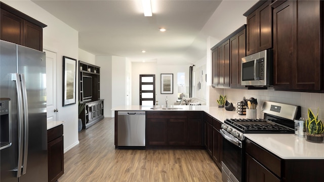 kitchen with kitchen peninsula, stainless steel appliances, light wood-type flooring, dark brown cabinetry, and sink