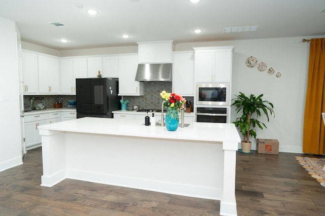 kitchen featuring oven, built in microwave, an island with sink, black refrigerator, and white cabinets