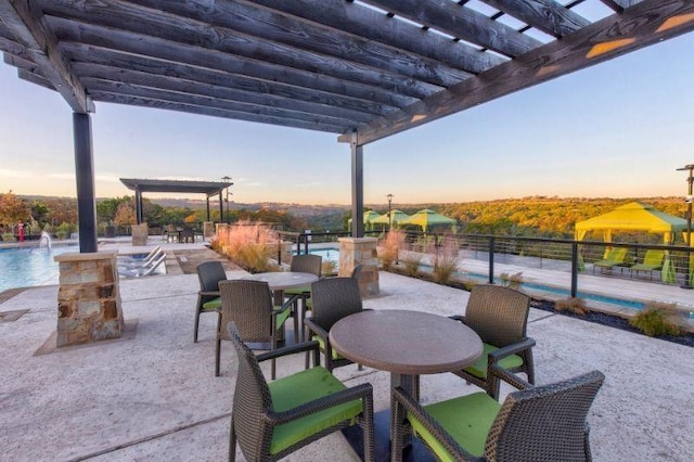 patio terrace at dusk featuring pool water feature, a pergola, and a community pool