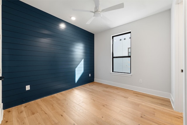 unfurnished room with ceiling fan, light wood-type flooring, and wood walls