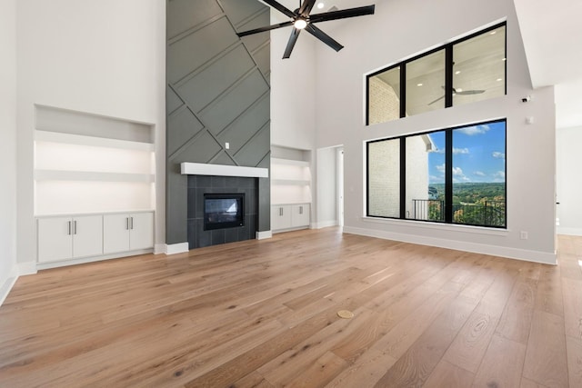 unfurnished living room featuring ceiling fan, a tiled fireplace, a high ceiling, and light hardwood / wood-style floors