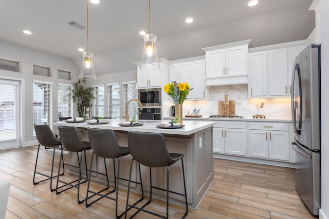 kitchen featuring decorative light fixtures, decorative backsplash, white cabinetry, appliances with stainless steel finishes, and an island with sink