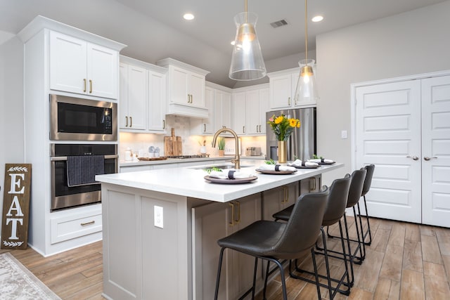 kitchen featuring white cabinetry, stainless steel appliances, light hardwood / wood-style floors, sink, and a center island with sink