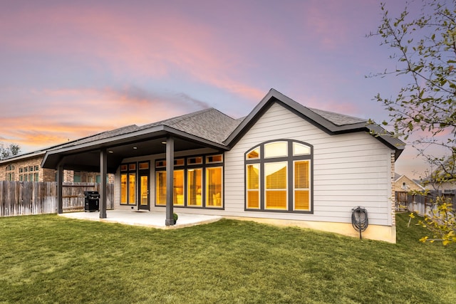 back house at dusk with a lawn and a patio