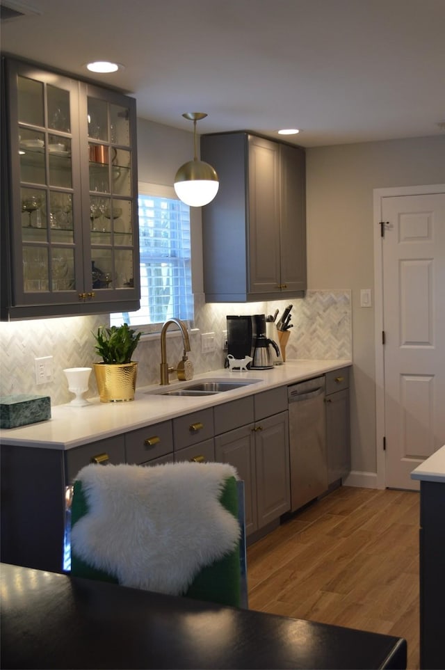 kitchen with gray cabinetry, dishwasher, hanging light fixtures, light hardwood / wood-style flooring, and sink