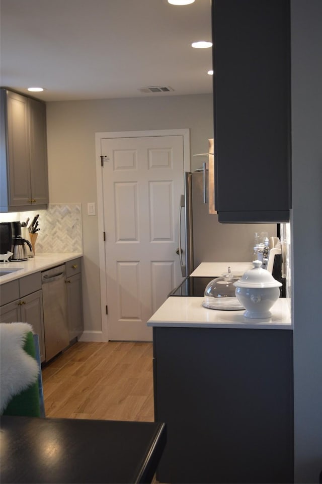 kitchen featuring tasteful backsplash, dishwasher, gray cabinets, and light hardwood / wood-style floors