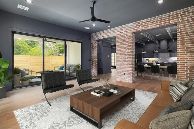 living room with ceiling fan, wood-type flooring, and brick wall