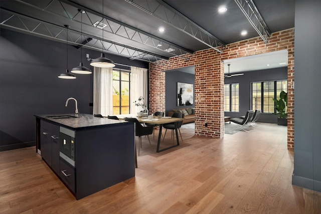 kitchen with a center island with sink, pendant lighting, sink, light hardwood / wood-style flooring, and brick wall