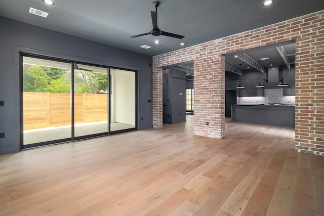 unfurnished living room featuring ceiling fan, light wood-type flooring, and brick wall