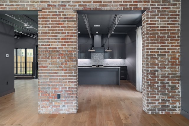 kitchen with gas stovetop, backsplash, wall chimney range hood, and light wood-type flooring