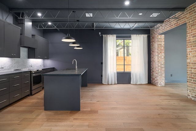 kitchen featuring a center island with sink, electric range, brick wall, pendant lighting, and light hardwood / wood-style flooring