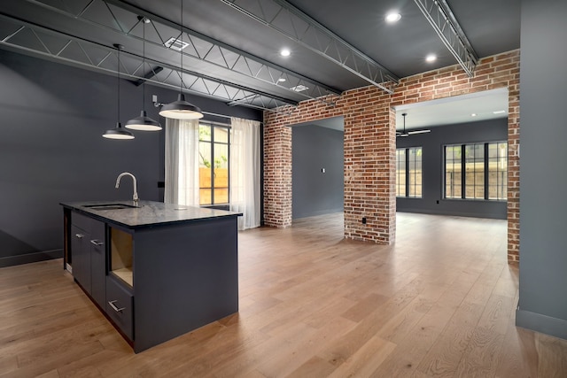 kitchen featuring hardwood / wood-style floors, an island with sink, decorative light fixtures, brick wall, and sink